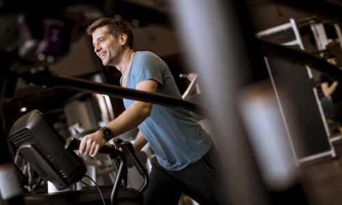 Young man doing exercise on elliptical cross trainer in sport fitness gym club
