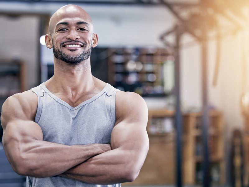Portrait of a muscular young man standing with his arms crossed in a gym.